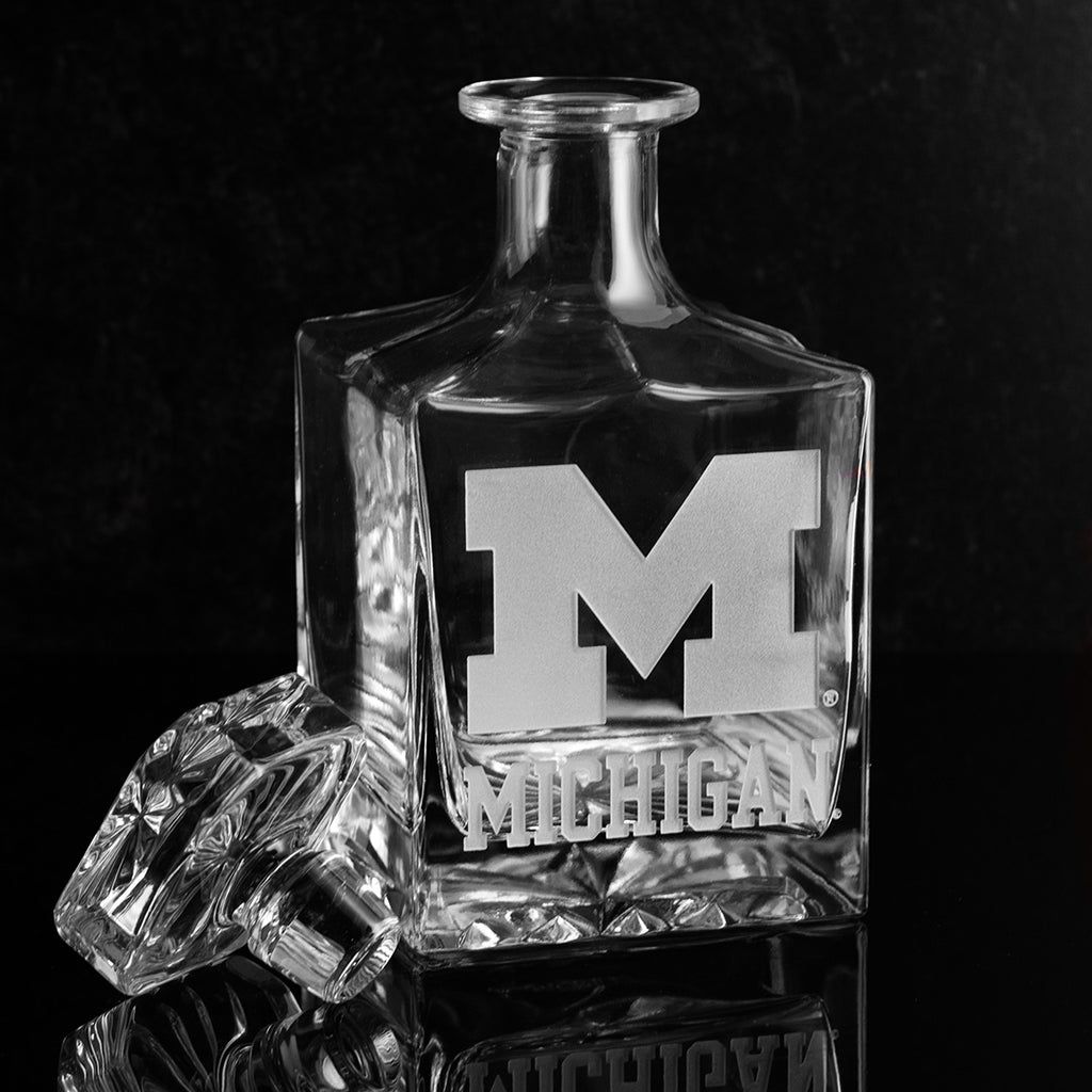 A clear crystal glass decanter with University of Michigan logo etched into the glass