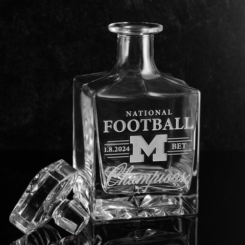 A clear crystal glass decanter with University of Michigan logo and National Football Champions etched into the glass