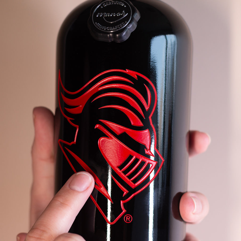 Hand holding up Rutgers University Scarlet Knight Etched Wine bottle from Mano's Wine with finger pointing to Scarlet Knight logo