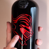 Hand holding up Rutgers University Scarlet Knight Etched Wine bottle from Mano's Wine with finger pointing to Scarlet Knight logo