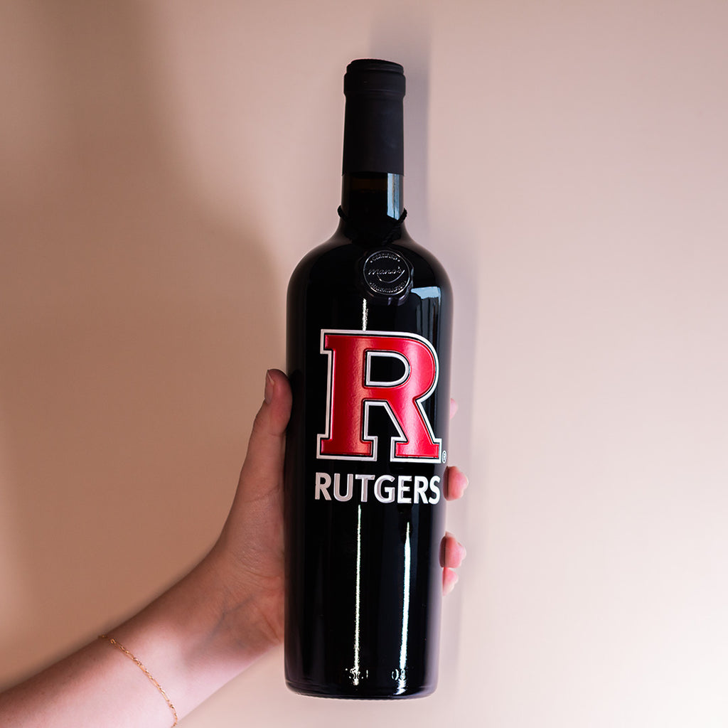 Hand holding up Rutgers University red R wine bottle