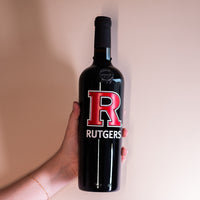 Hand holding up Rutgers University red R wine bottle