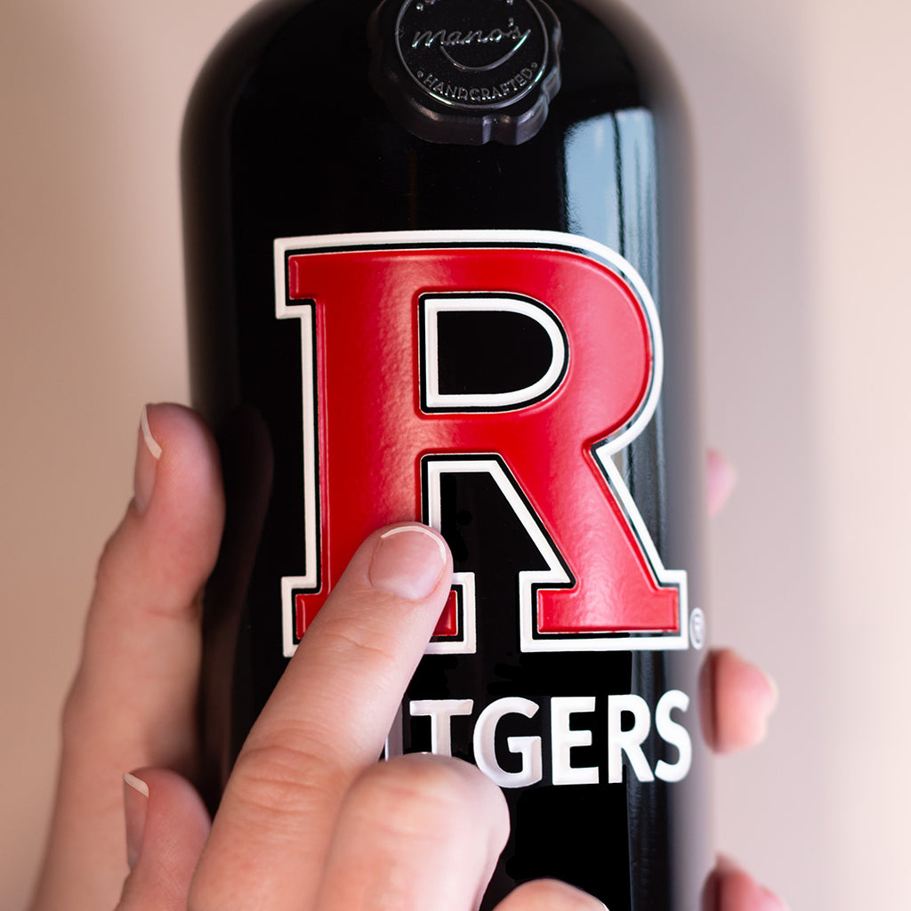 Bottle of Rutgers University wine held by a hand with a red 'R' logo on the Mano's Wine bottle
