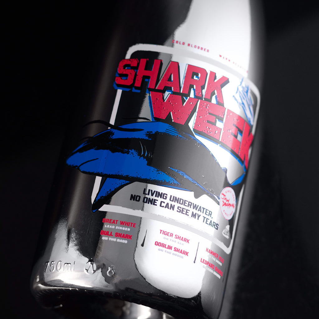 Close up of Mano's Wine bubbly bottle featuring red and blue Shark Week design