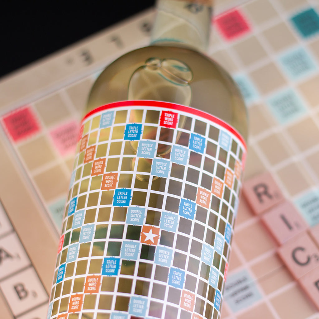 Close up of a bottle of Mano's Wine with a colorful Scrabble board label on top of a Scrabble board