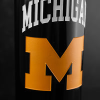 Close up of a Michigan logo with a large gold 'M' etched on a Mano's Wine bottle